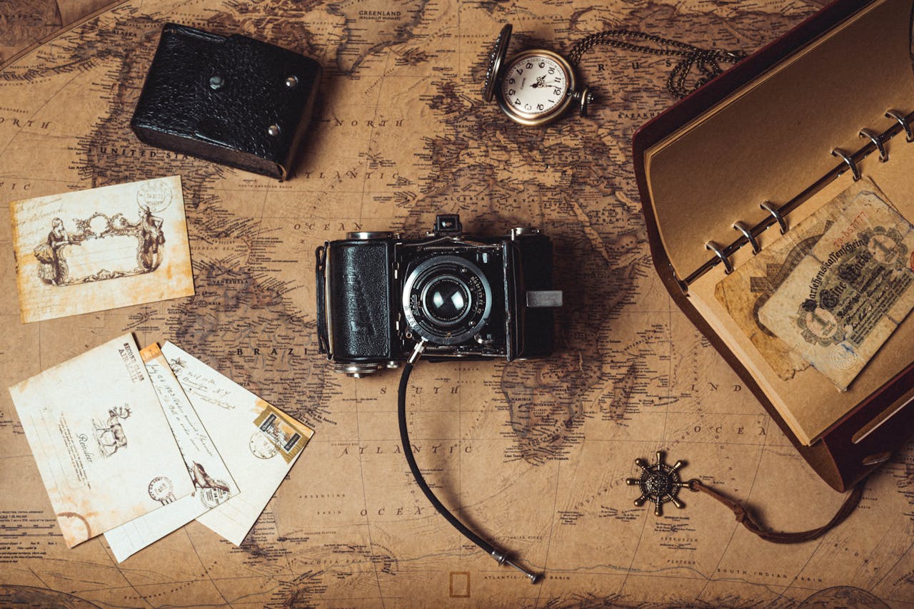 heros-img A nostalgic flat lay combining vintage travel items, an analog camera, and a world map.